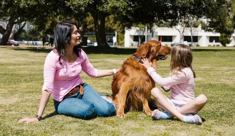 Une femme et un enfant assis dans un parc avec leur chien.